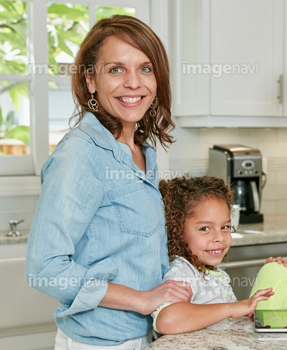 Side view of mother behind daughter in kitchen looking at camera smiling