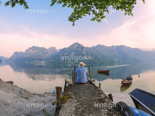 Italy, Lombardy, back view of man sitting on jetty at Lake Idro at morning twilight